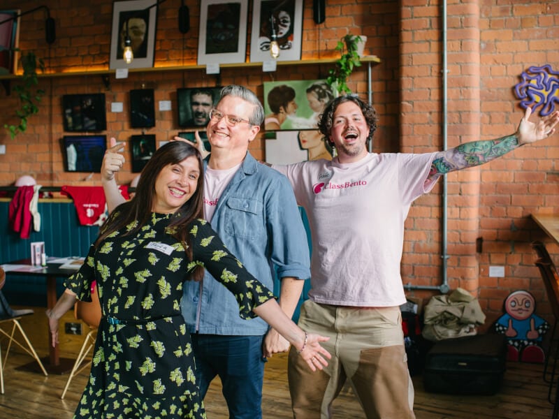 A woman and two men are smiling for a picture with their arms outstretched
